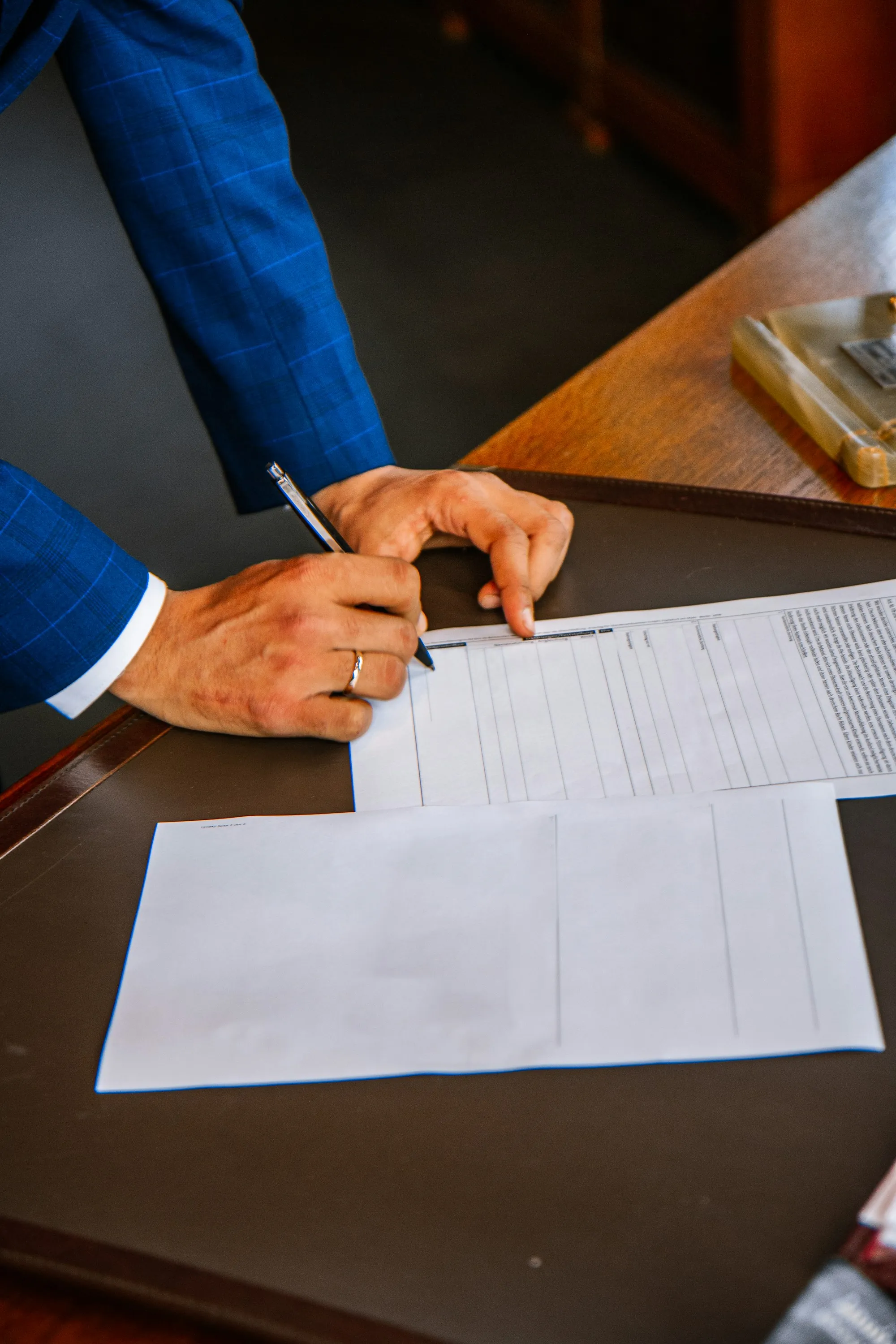 Hand signing a contract beside a stack of papers